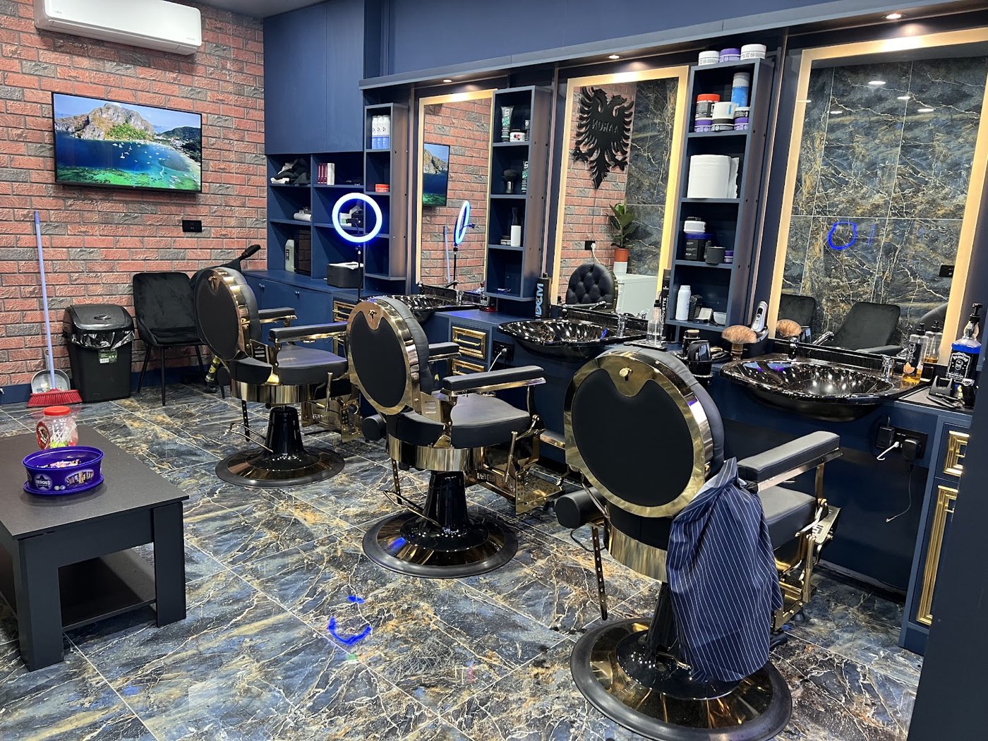 Inside Aaron Barber in Manor Park: brass and black barber chairs, navy cabinets and marble tiling
